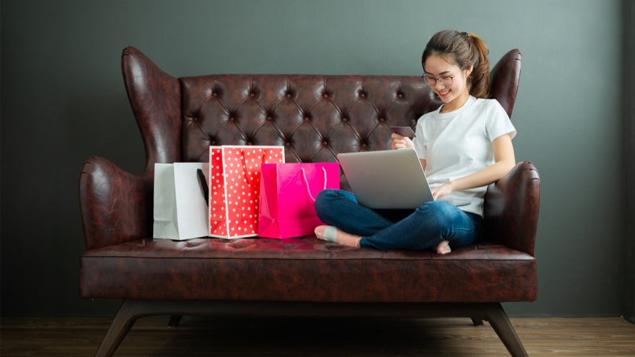 Smiling woman sitting on sofa doing online shopping on laptop; image used for HSBC Singapore  Tips for safe online shopping article.