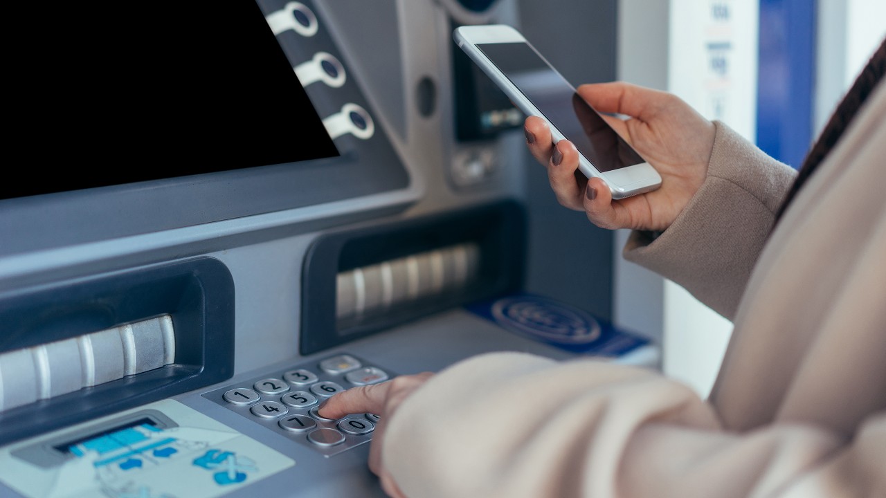 Using ATM with mobile phone; image used for HSBC Singapore Cybersecurity tips safe travels article.
