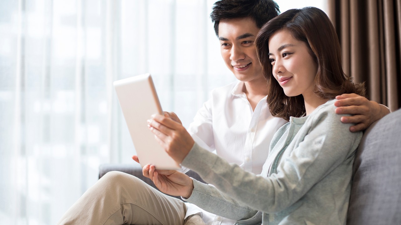 Couple sitting on sofa with tablet; image used for HSBC Singapore 5 Things You Didn’t Know About Debt Consolidation article. 