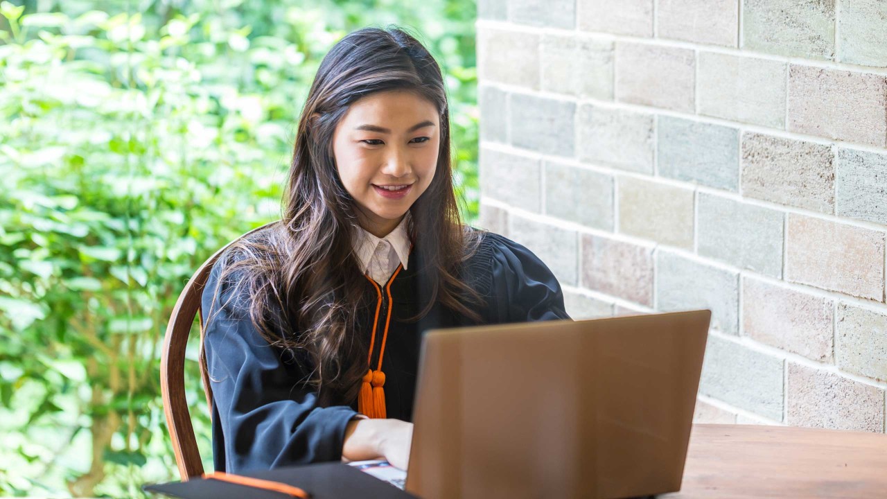 穿着毕业礼服的女学生正在使用笔记本电脑。