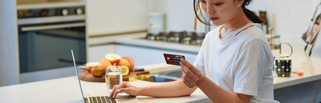 一位女士正在使用银行卡和笔记本电脑；图片使用于汇丰多币种借记卡。